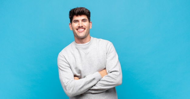 Jovem bonito parecendo um empreendedor feliz, orgulhoso e satisfeito, sorrindo com os braços cruzados