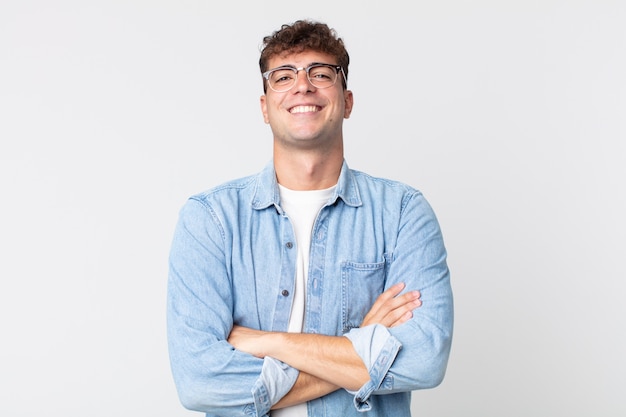 Jovem bonito parecendo um empreendedor feliz, orgulhoso e satisfeito, sorrindo com os braços cruzados