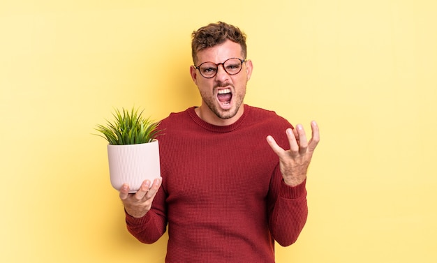 Jovem bonito parecendo zangado, irritado e frustrado. conceito de planta decorativa