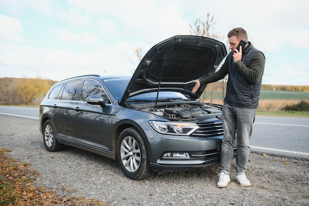 Jovem bonito pedindo ajuda com seu carro quebrado na beira da estrada