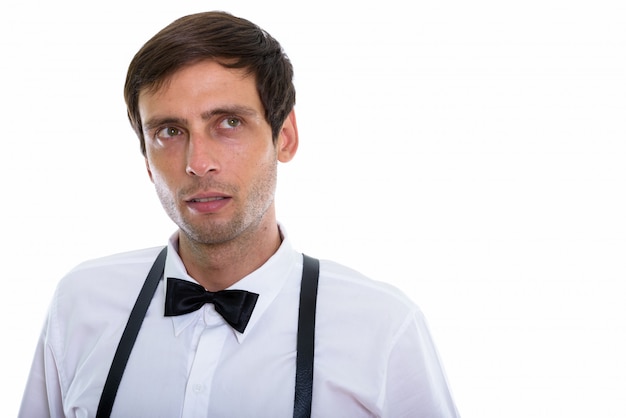 jovem bonito pensando e olhando para cima enquanto usava suspensórios e gravata borboleta