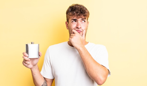 Jovem bonito pensando sentindo o conceito de frasco de álcool duvidoso e confuso