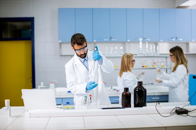 Jovem bonito pesquisador em roupas de trabalho de proteção em frasco de análise de laboratório