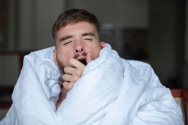 Jovem bonito preguiçoso cansado cara sonolento está bocejando cobertor na cama no quarto no início da manhã esticando as mãos corpo Bom dia acordando