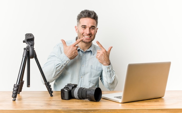 Jovem bonito professor de fotografia sorri, apontando o dedo para a boca.