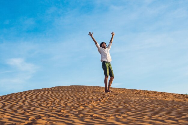 Jovem bonito pulando descalço na areia no deserto, curtindo a natureza e o sol. Diversão, alegria e liberdade.
