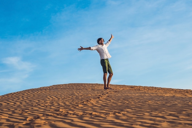 Jovem bonito pulando descalço na areia no deserto, curtindo a natureza e o sol. Diversão, alegria e