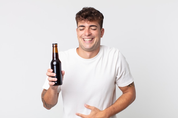 Jovem bonito rindo alto de uma piada hilária e segurando uma garrafa de cerveja