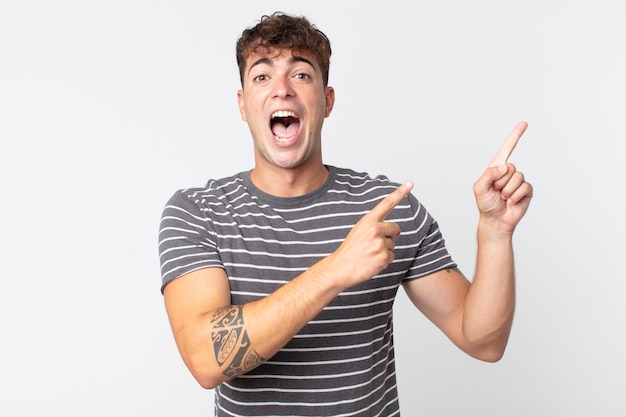 Jovem bonito se sentindo alegre e surpreso, sorrindo com uma expressão chocada e apontando para o lado