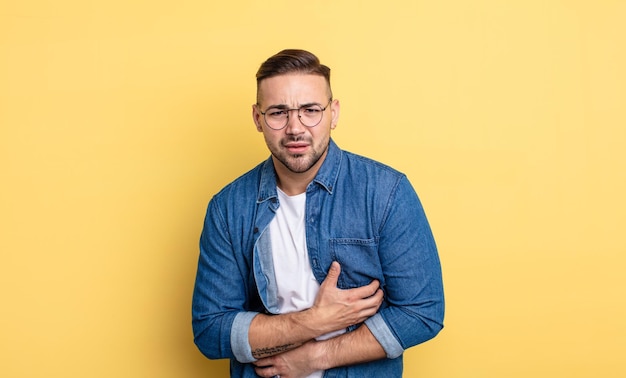 Jovem bonito se sentindo ansioso, doente, doente e infeliz, sofrendo uma dor de estômago dolorosa ou gripe