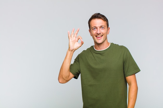 Jovem bonito se sentindo bem-sucedido e satisfeito, sorrindo com a boca bem aberta