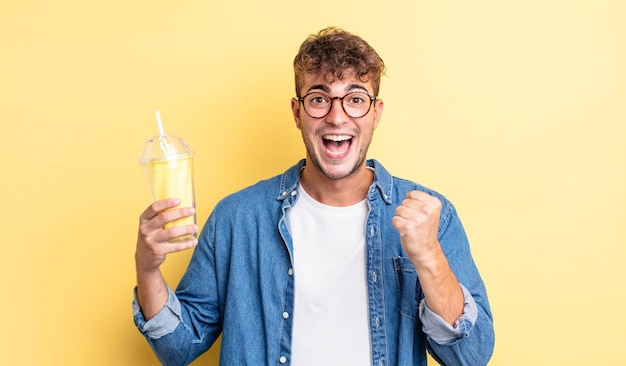 Jovem bonito se sentindo chocado, rindo e comemorando o sucesso. conceito de milkshake