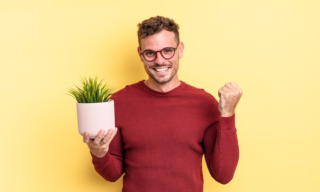 Jovem bonito se sentindo chocado, rindo e comemorando o sucesso. conceito de planta decorativa