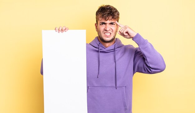 Jovem bonito se sentindo confuso e perplexo, mostrando que você é louco. copie o conceito de espaço