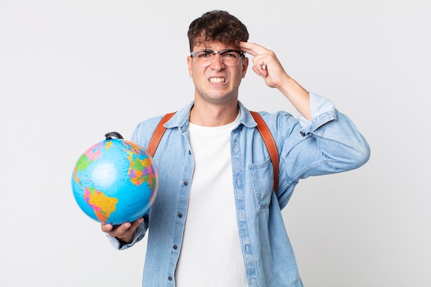 jovem bonito se sentindo confuso e perplexo, mostrando que você é louco. estudante segurando um mapa do globo