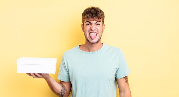 Jovem bonito se sentindo enojado e irritado e com a língua de fora. conceito de caixa branca