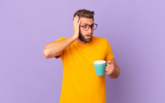 Jovem bonito se sentindo feliz, animado e surpreso. e segurando uma caneca de café