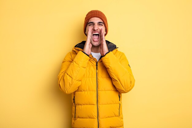 Jovem bonito se sentindo feliz, dando um grande grito com as mãos ao lado da boca. conceito de inverno