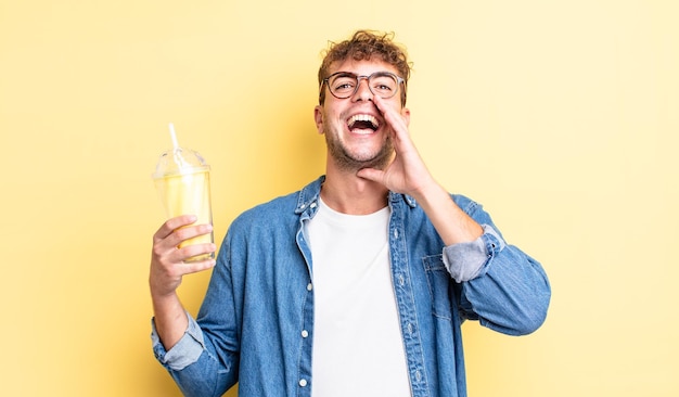 Jovem bonito se sentindo feliz dando um grande grito com as mãos ao lado do conceito de milk-shake de boca