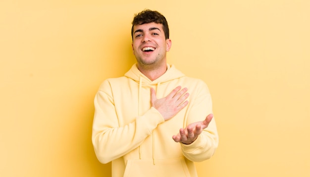 Jovem bonito se sentindo feliz e apaixonado sorrindo com uma mão ao lado do coração e a outra esticada na frente