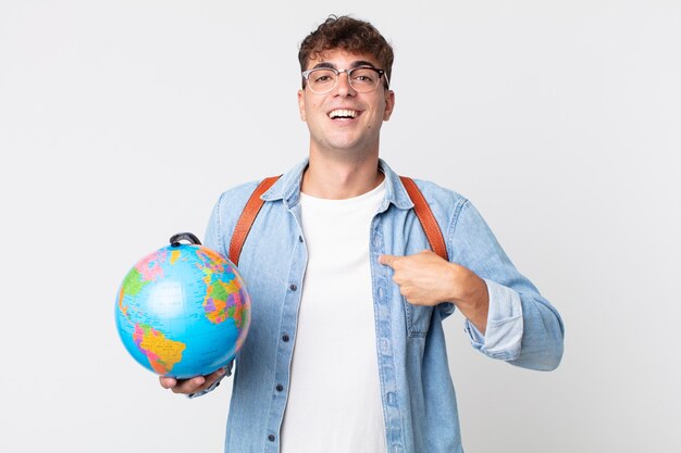 Jovem bonito se sentindo feliz e apontando para si mesmo com um animado. estudante segurando um mapa do globo