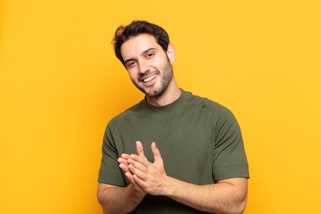 Jovem bonito se sentindo feliz e bem-sucedido, sorrindo e batendo palmas, dizendo parabéns com aplausos