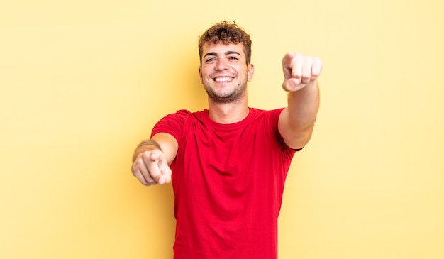 Jovem bonito se sentindo feliz e confiante, apontando para a câmera com as duas mãos e rindo, escolhendo você