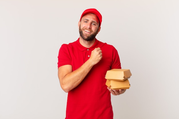 Jovem bonito se sentindo feliz e enfrentando um desafio ou celebrando o conceito de entrega de hambúrguer