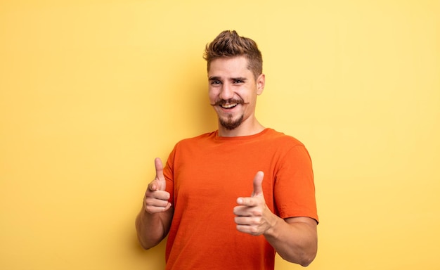 Jovem bonito se sentindo feliz legal satisfeito relaxado e bem sucedido apontando para a câmera escolhendo seu estranho conceito de bigode