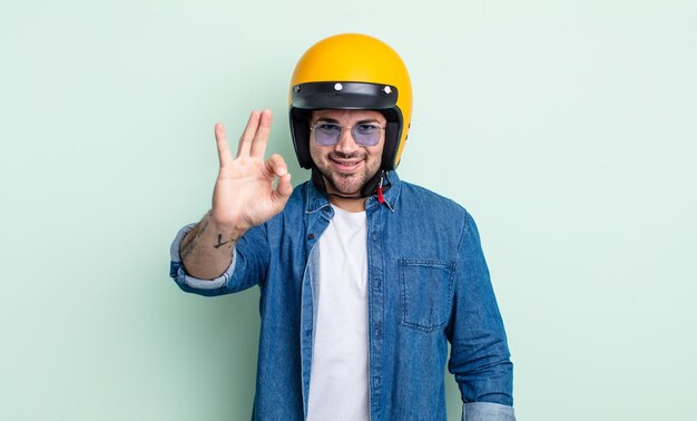 Jovem bonito se sentindo feliz, mostrando aprovação com um gesto certo. conceito de capacete de motocicleta