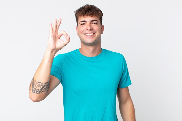 Jovem bonito se sentindo feliz, relaxado e satisfeito, mostrando aprovação com um gesto de ok, sorrindo