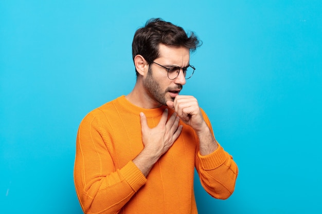 Jovem bonito se sentindo mal com dor de garganta e sintomas de gripe, tosse com a boca coberta