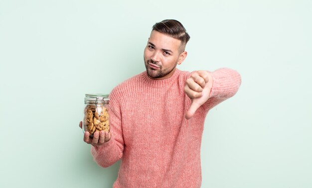 Jovem bonito se sentindo mal, mostrando os polegares para baixo. conceito de garrafa de biscoitos