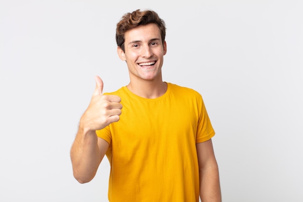 Jovem bonito se sentindo orgulhoso, despreocupado, confiante e feliz, sorrindo positivamente com os polegares para cima