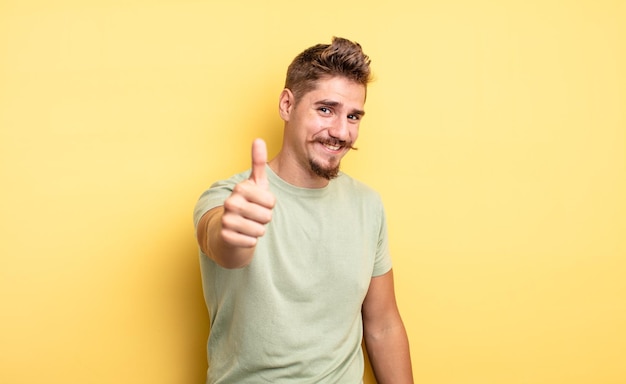 Jovem bonito se sentindo orgulhoso despreocupado confiante e feliz sorrindo positivamente com polegares para cima conceito de bigode estranho