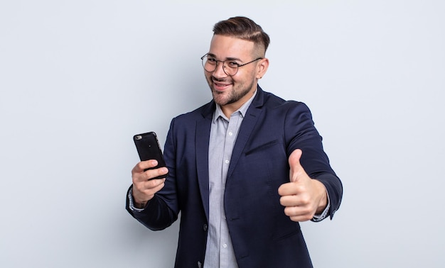 Jovem bonito se sentindo orgulhoso, sorrindo positivamente com o polegar para cima conceito de negócios e smartphone