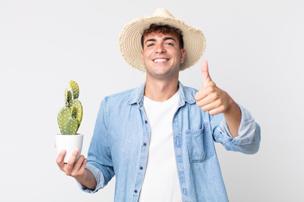 jovem bonito se sentindo orgulhoso, sorrindo positivamente com o polegar para cima. fazendeiro segurando um cacto decorativo