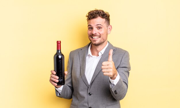 Jovem bonito se sentindo orgulhoso, sorrindo positivamente com o polegar para cima. garrafa de vinho conceito