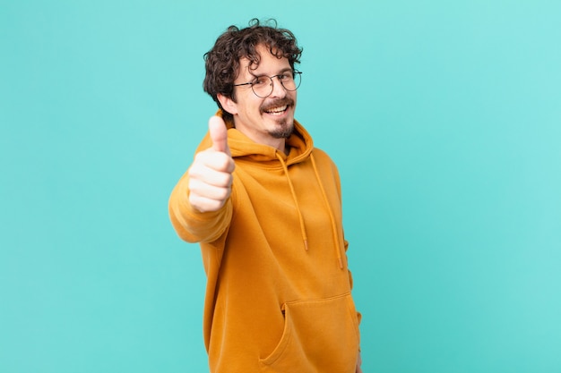 Jovem bonito se sentindo orgulhoso, sorrindo positivamente com o polegar para cima