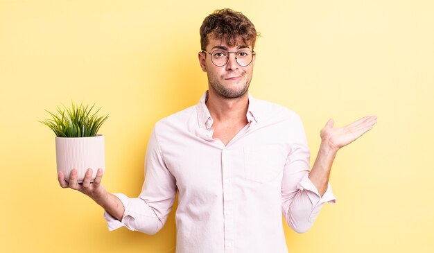 Jovem bonito se sentindo perplexo, confuso e duvidoso. conceito de planta decorativa