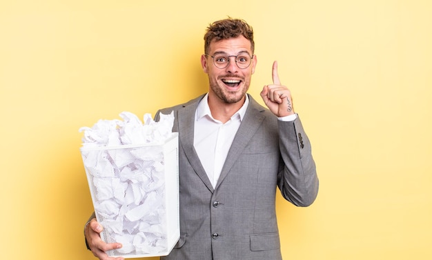 Jovem bonito se sentindo um gênio feliz e animado depois de perceber um conceito de lixo de bolas de papel de ideia