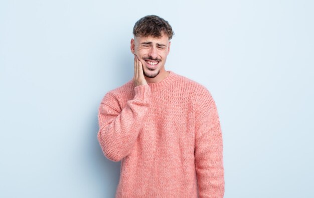 Jovem bonito segurando a bochecha e sofrendo de uma dor de dente dolorosa, sentindo-se doente, miserável e infeliz, procurando um dentista