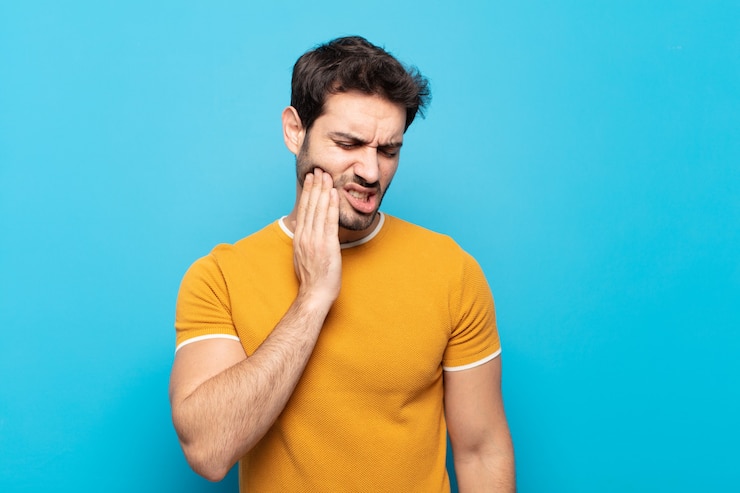 Foto jovem bonito segurando a bochecha e sofrendo dor de dente dolorosa, sentindo-se doente, miserável e infeliz, procurando um dentista