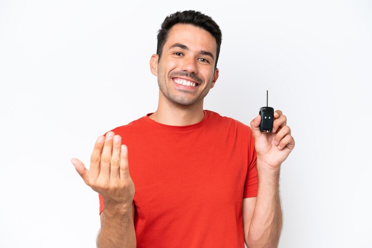 Foto jovem bonito segurando as chaves do carro sobre fundo branco isolado convidando para vir com a mão feliz que você veio