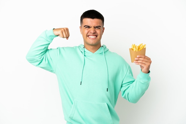 Jovem bonito segurando batatas fritas sobre um fundo branco isolado, fazendo um gesto forte