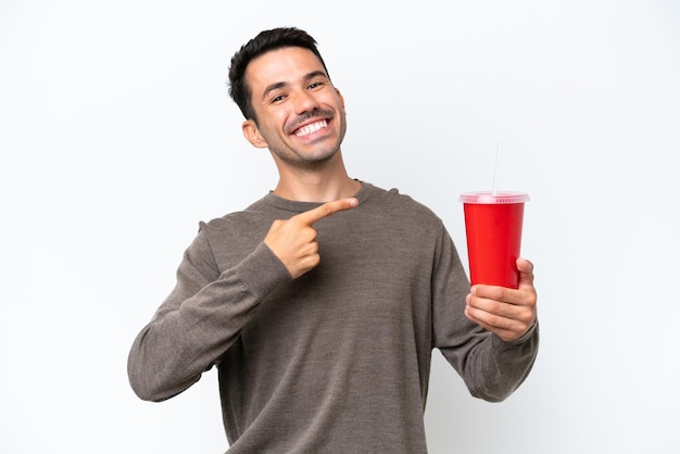 Jovem bonito segurando refrigerante sobre fundo branco isolado e apontando-o