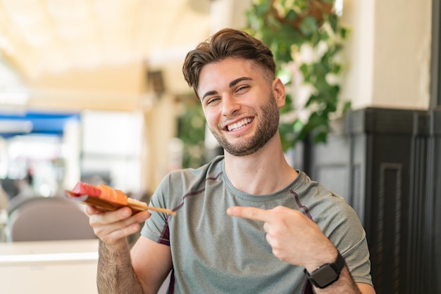 Jovem bonito segurando sashimi ao ar livre e apontando-o