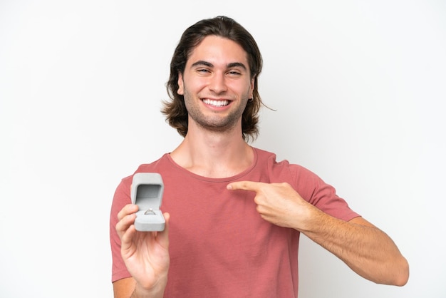 Jovem bonito segurando um anel de noivado isolado no fundo branco e apontando-o