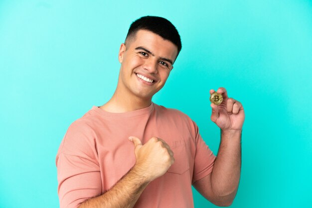 Jovem bonito segurando um Bitcoin sobre um fundo azul isolado, orgulhoso e satisfeito