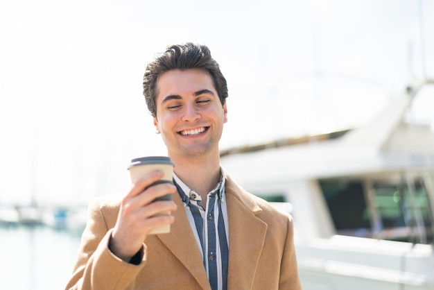 Jovem bonito segurando um café para viagem ao ar livre com expressão feliz